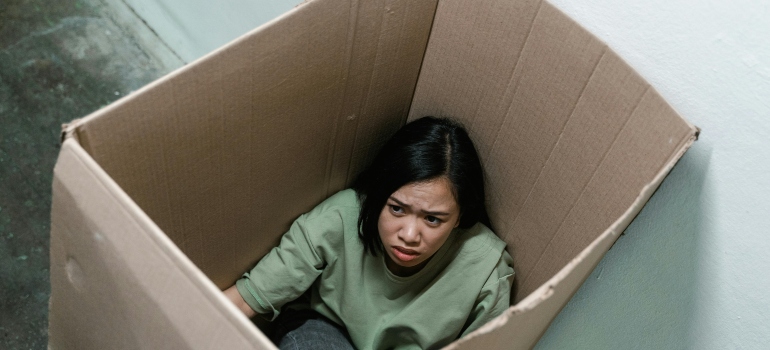 A woman in a green blouse is sitting in the cartoon box and having a panic attack.