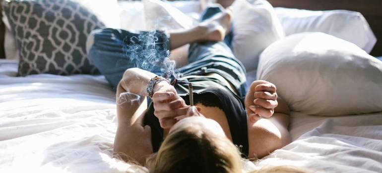 A woman is lying on the bed and smoking marijuana.