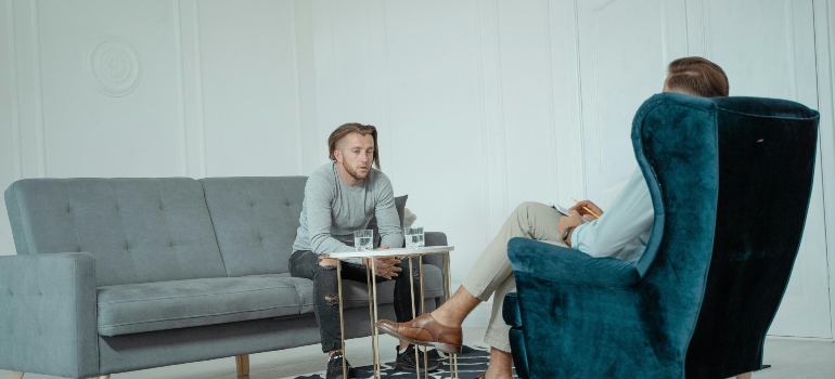 A man is sitting on the couch and talking to his therapist about sleeping problems.