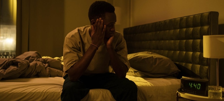 a man with sleeping issues sitting on the bed and looking at the clock