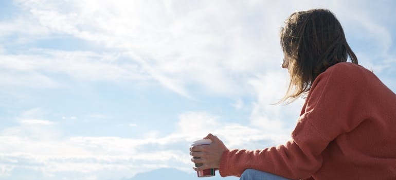 Woman holding a cup of coffee and looking at the sky.