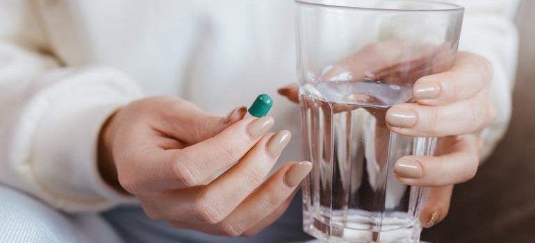 Woman holding a glass of water and a pill.