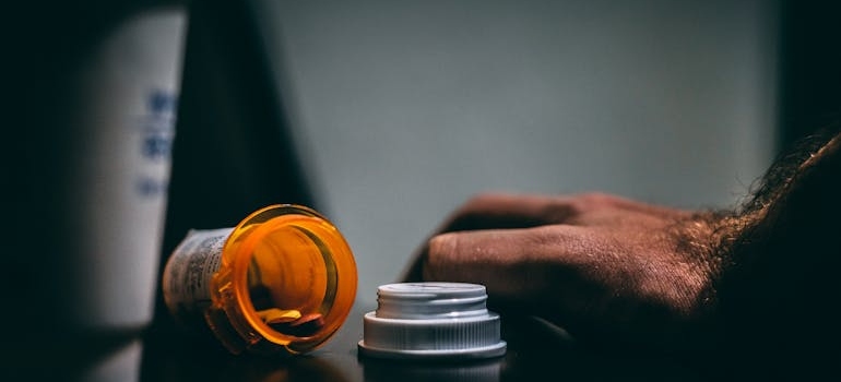 Almost empty pill bottle next to a man's hand.