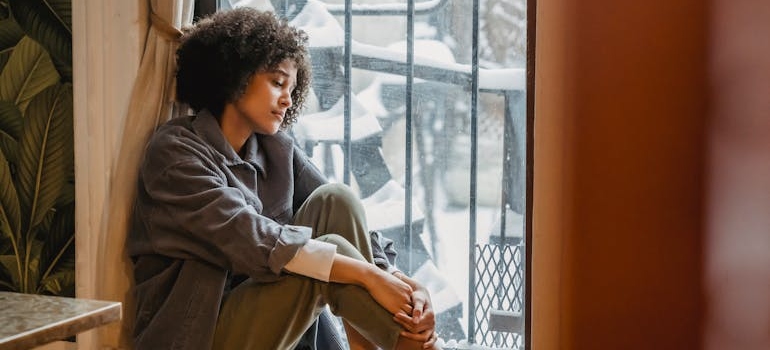 A woman with a sad expression sitting on a windowsill.