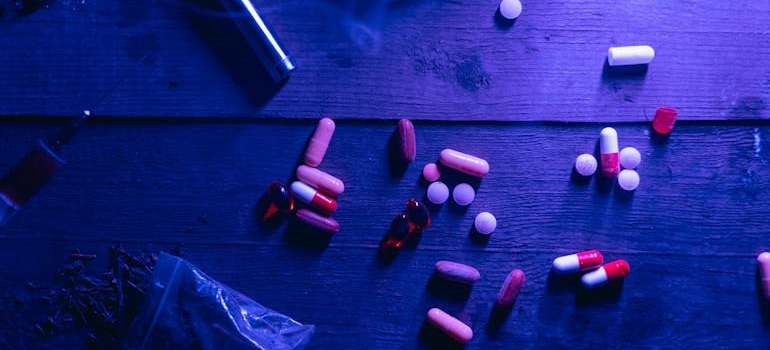 Pills, syringe and other drugs on a wooden surface.