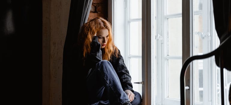 Woman sitting by a windowsill thinking about the difference between social drinking vs alcoholism.