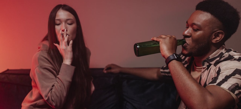 A couple sitting next to each other and drinking and smoking