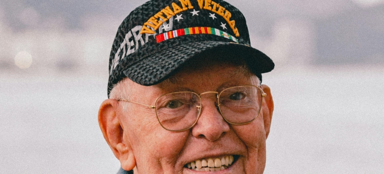 An old man with glasses is smiling and wearing a Vietnam veteran cap.