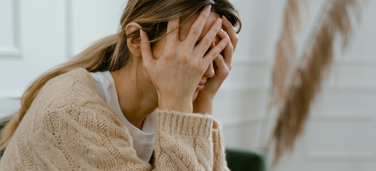 A woman is sitting on the green couch, covering her face with her hands and thinking about overcoming Precipitated Withdrawal.