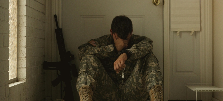 A veteran soldier is sitting on the floor and covering his face with his hand.