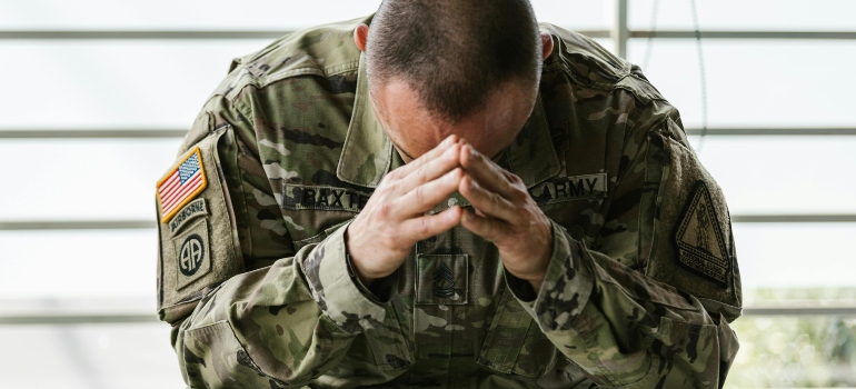 A veteran is sitting in a chair, holding his head down, and thinking about why Veterans struggle to seek rehab.